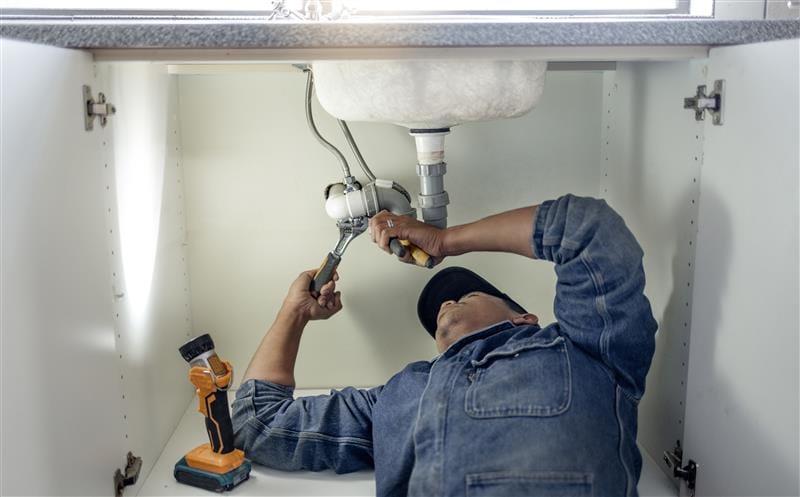 Plumber repairing pipes beneath a bathroom sink in Murray