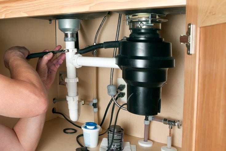 Plumber repairing a garbage disposal beneath a kitchen sink in Murray