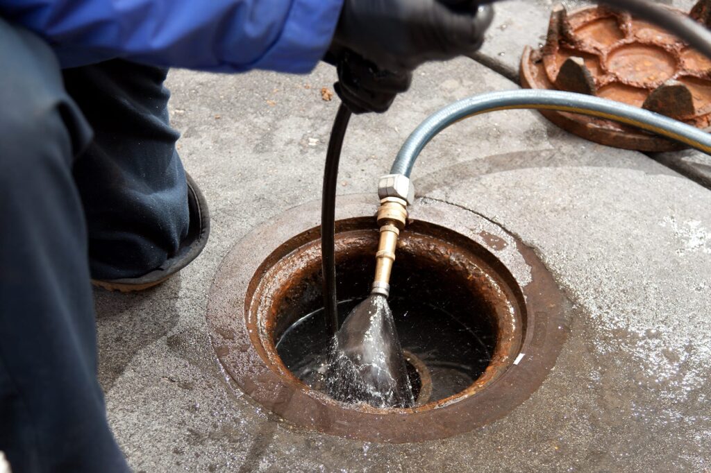 Plumber hydro jetting a sewer line through a manhole in Murray