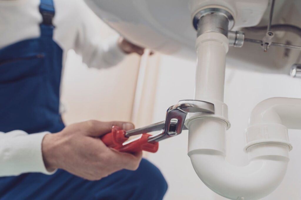 Plumber repairing a white drain pipe beneath a sink in Murray