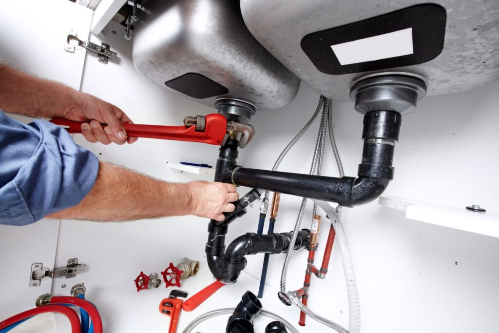 Plumber repairing drain pipes beneath a kitchen sink in Murray